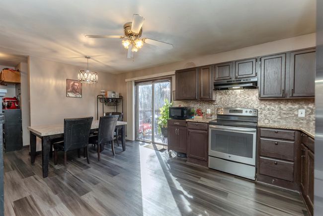 Kitchen with tasteful backsplash, black microwave, electric range, under cabinet range hood, and ceiling fan with notable chandelier | Image 13