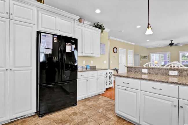 Kitchen with freestanding refrigerator, a ceiling fan, white cabinetry, decorative light fixtures, and crown molding | Image 11