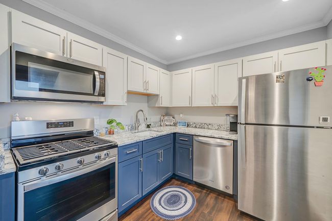 Kitchen with crown molding, blue cabinets, a sink, white cabinets, and appliances with stainless steel finishes | Image 17