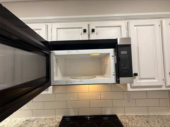 Kitchen view of white cabinetry, light countertops, white microwave, and backsplash | Image 16