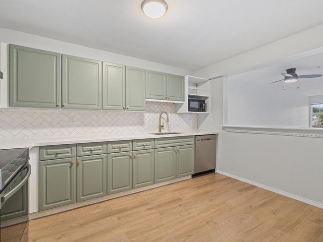 Kitchen with green cabinetry, light countertops, a sink, open shelves, and black appliances | Image 4