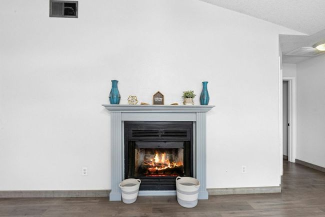 Detailed view of a warm lit fireplace, a textured ceiling, and wood finished floors | Image 9