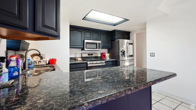 Kitchen featuring light tile patterned floors, stainless steel appliances, dark stone countertops, a sink, and a peninsula | Image 9