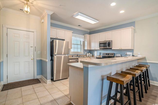 Kitchen featuring stainless steel appliances, a peninsula, baseboards, a kitchen breakfast bar, and crown molding | Image 6