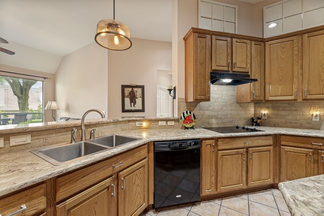 Kitchen with black appliances, under cabinet range hood, a sink, decorative backsplash, and light tile patterned floors | Image 16