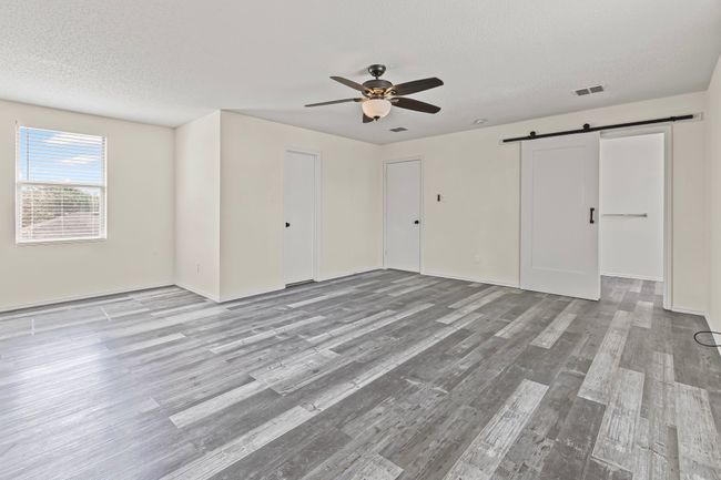 Unfurnished bedroom featuring a barn door, wood finished floors, a textured ceiling, and ceiling fan | Image 16