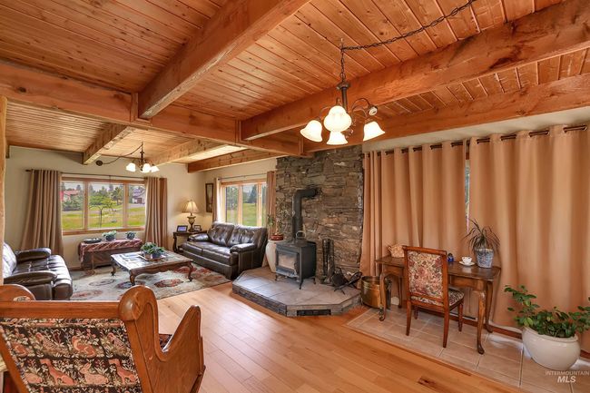 Living area with a chandelier, a wood stove, a wooden ceiling with exposed beams, and wood-type flooring | Image 13