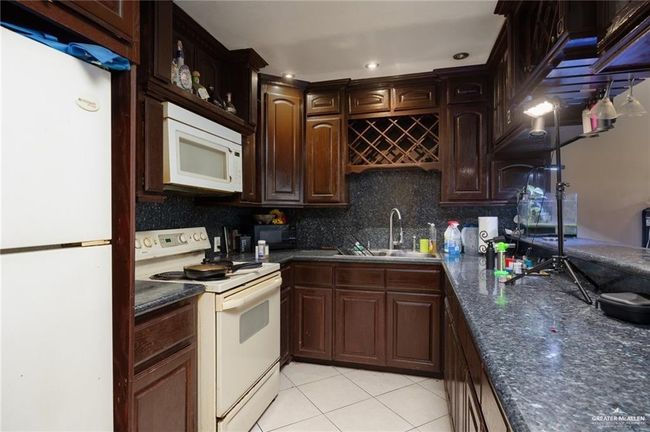 Kitchen featuring backsplash, white appliances, dark brown cabinetry, sink, and light tile patterned floors | Image 14