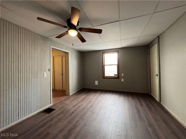 Unfurnished room featuring a paneled ceiling, wood finished floors, a ceiling fan, visible vents, and baseboards | Image 10