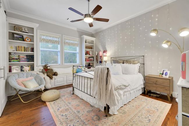 This beautifully appointed room features rich wood floors, tall ceilings, crown moulding, and a sleek, modern ceiling fan. Custom built-ins elegantly frame a pair of large windows, which include a charming window seat beneath—perfect for reading or relaxing. | Image 31