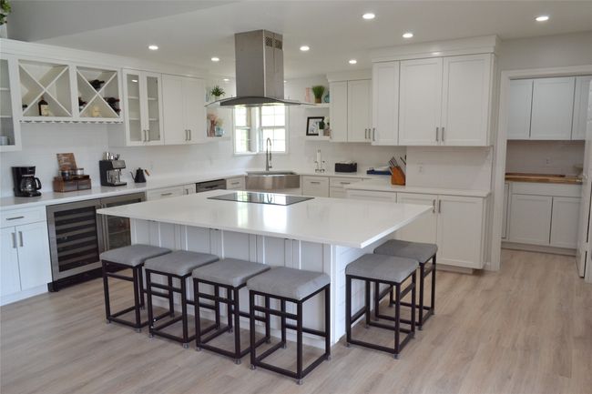 Kitchen featuring island exhaust hood, beverage cooler, open shelves, a breakfast bar, and recessed lighting | Image 7