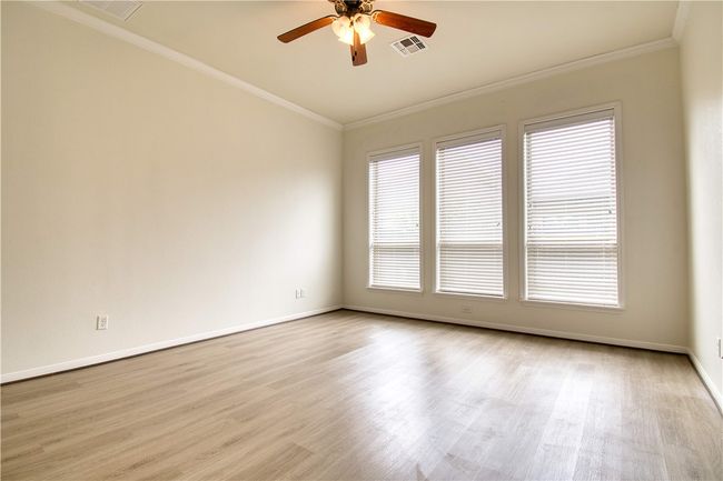 Spare room featuring crown molding, light wood-type flooring, baseboards, visible vents, and ceiling fan | Image 14