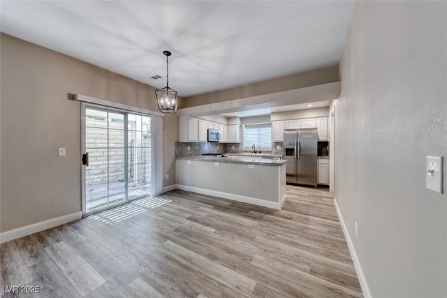 Kitchen with appliances with stainless steel finishes, white cabinetry, a peninsula, a chandelier, and light wood-style flooring | Image 9