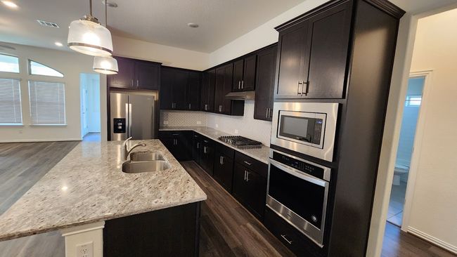 Kitchen featuring stainless steel appliances, a sink, dark wood-style flooring, a kitchen island with sink, and tasteful backsplash | Image 7