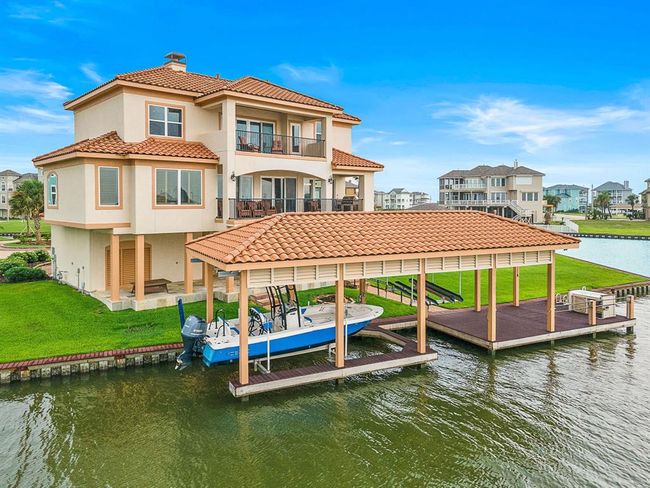 This Mediterranean-style waterfront home blends coastal elegance with relaxed luxury. With terracotta roof tiles, stucco exterior, and spacious balconies, it offers stunning canal views. Highlights include a covered patio, upper terrace, private boat slip with lift, and beautifully landscaped grounds—perfect for indoor-outdoor living and entertaining | Image 45