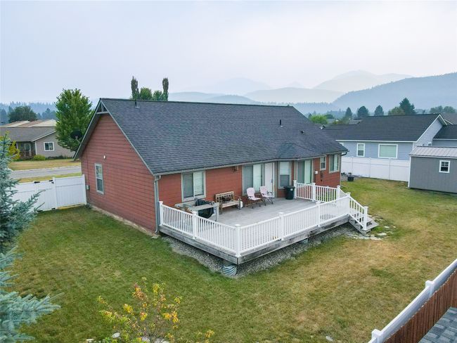 Back of property featuring a fenced backyard, a deck with mountain view, a lawn, and roof with shingles | Image 25