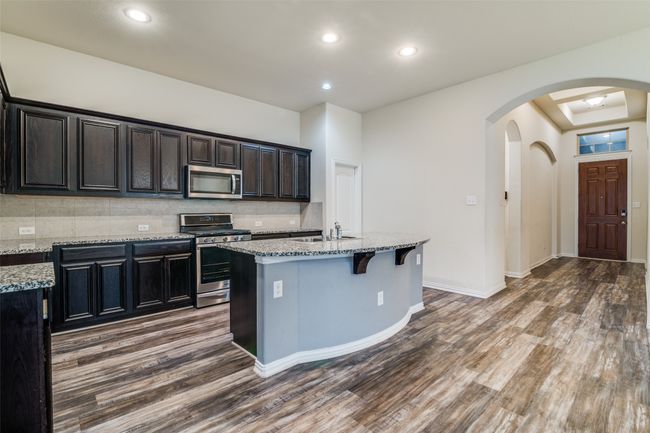 Kitchen with stainless steel appliances, dark wood-type flooring, arched walkways, light stone countertops, and tasteful backsplash | Image 11