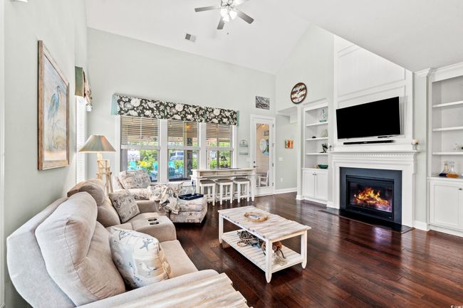 Living area with high vaulted ceiling, a ceiling fan, wood-type flooring, a glass covered fireplace, and built in shelves | Image 15