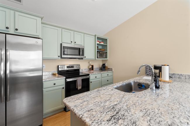 Kitchen featuring appliances with stainless steel finishes, a sink, vaulted ceiling, light stone countertops, and a peninsula | Image 7