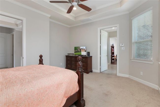 This photo showcases a cozy bedroom with neutral tones, featuring a tray ceiling with a fan, a large window for natural light. | Image 27