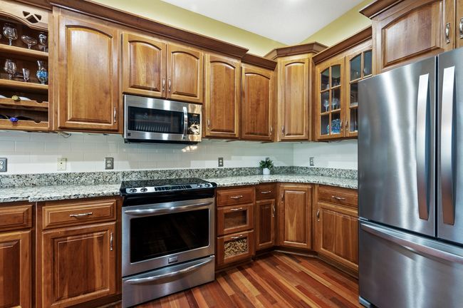 Granite countertops are a perfect accent to the warmth of the woodwork and designer tile backsplash. Enjoy a new stainless French door refrigerator & range (2022). Quality custom cabinetry includes glass door fronts, wine storage & crown molding. | Image 12