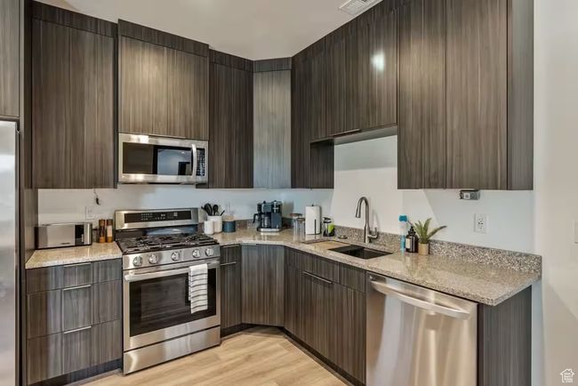 Kitchen with stainless steel appliances, a sink, light wood-type flooring, light stone countertops, and modern cabinets | Image 69