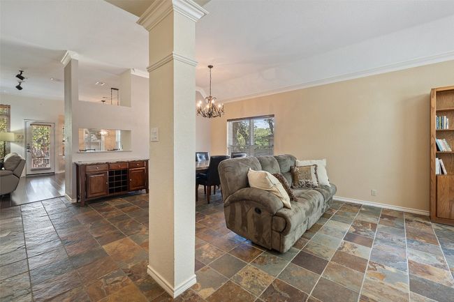 Living room with stone tile flooring, crown molding, a chandelier, baseboards, and ornate columns | Image 6