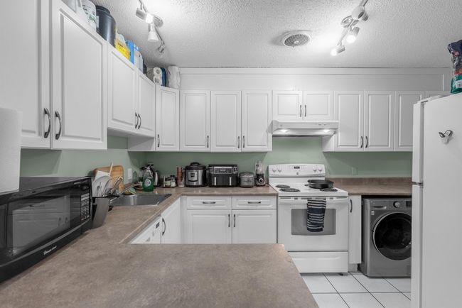 Kitchen featuring white appliances, white cabinetry, under cabinet range hood, washer / dryer, and a sink | Image 7