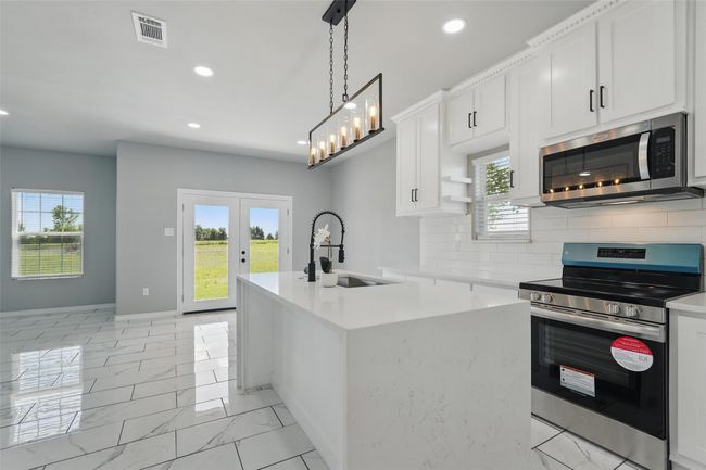Kitchen featuring decorative backsplash, appliances with stainless steel finishes, a sink, and visible vents | Image 8