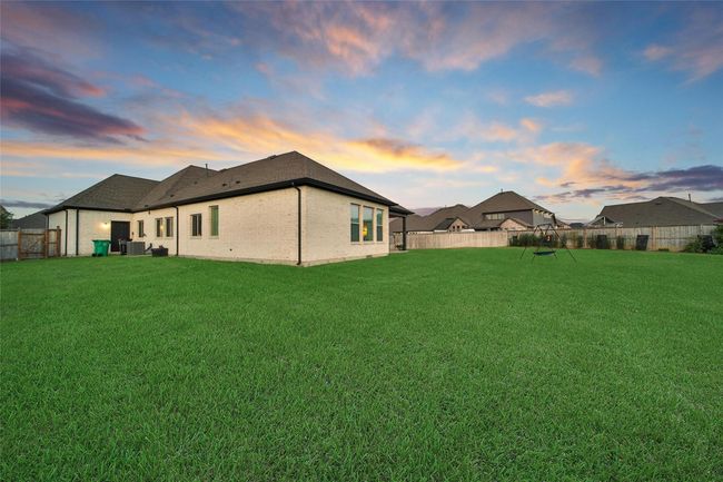 This photo showcases a spacious backyard with a well-maintained lawn, ideal for outdoor activities. The house features a modern design with a brick exterior, set against a picturesque sunset sky. | Image 44