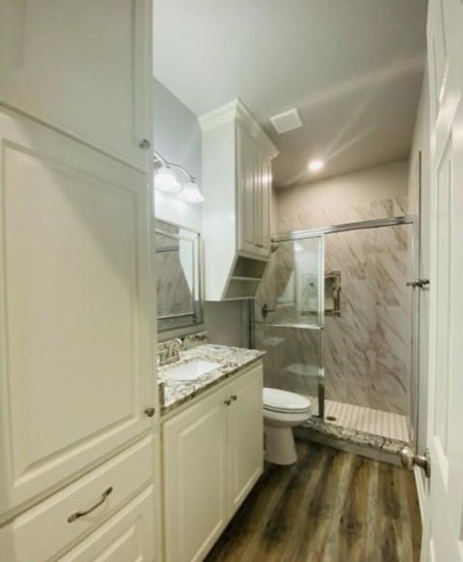 Bathroom featuring toilet, a marble finish shower, vanity, and wood finished floors | Image 8