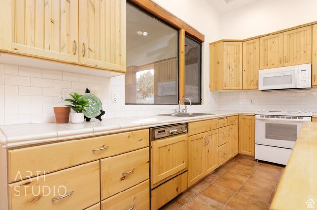 Kitchen featuring a sink, backsplash, light brown cabinets, and white appliances | Image 20