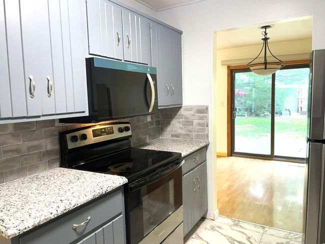 Kitchen with range with electric cooktop, gray cabinetry, freestanding refrigerator, and tasteful backsplash | Image 7