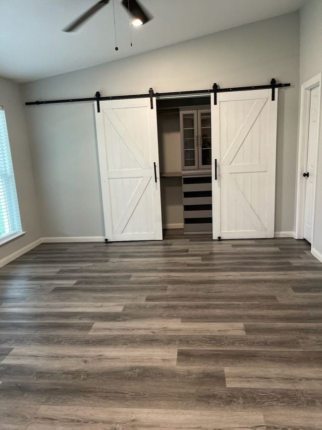 Unfurnished bedroom with dark hardwood / wood-style flooring, a barn door, ceiling fan, and vaulted ceiling | Image 10