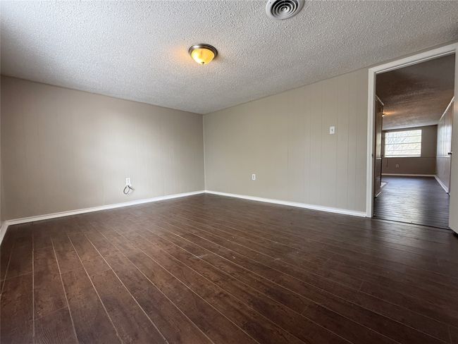 Empty room featuring dark wood-style floors, baseboards, a textured ceiling, and visible vents | Image 12