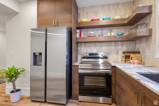 Kitchen with stainless steel appliances, open shelves, decorative backsplash, light stone counters, and light wood-style flooring | Image 59