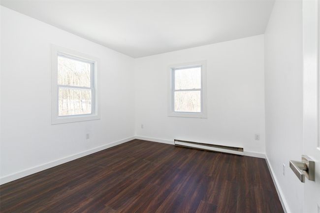 Empty bedroom featuring a baseboard heating unit, dark wood-style floors, and baseboards | Image 10