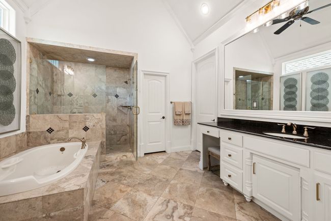 The Primary Bathroom features a vaulted ceiling, oversized jetted tub, a walk in tiled shower, framed mirrors, separate vanities, a ceiling fan, travertine tile flooring, winter gold fixtures and hardware and a private toilet closet. The wardrobe closet is quite spacious with off season storage racks and built ins. | Image 19