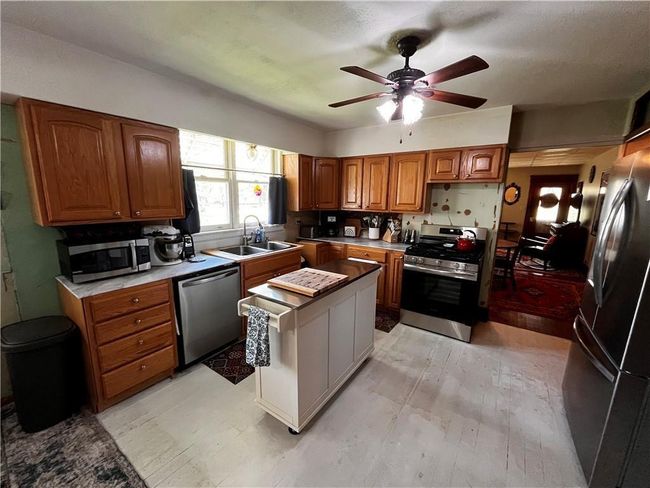 Kitchen with stainless steel appliances, brown cabinetry, a ceiling fan, a kitchen island, and light countertops | Image 7