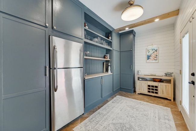 Kitchen featuring freestanding refrigerator, light tile patterned flooring, wood walls, beam ceiling, and open shelves | Image 13