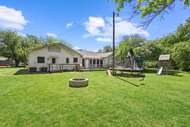 Rear view of property featuring central air condition unit, a playground, an outdoor fire pit, and a lawn | Image 35