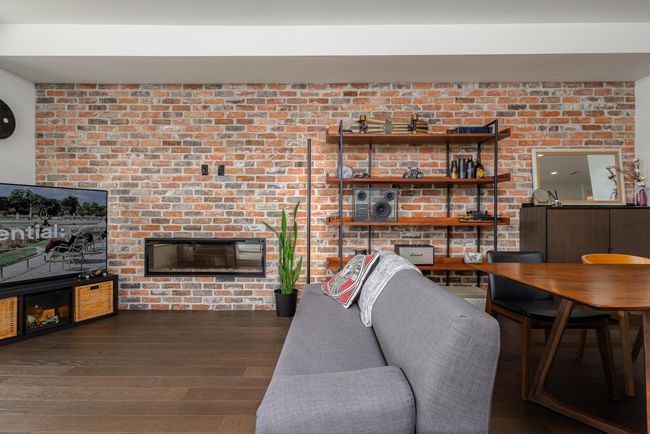 Living area featuring wood finished floors, a glass covered fireplace, and brick wall | Image 8