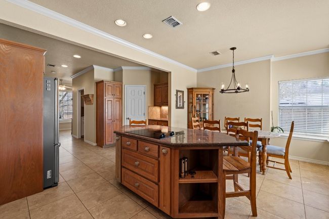 Kitchen with brown cabinetry, visible vents, an inviting chandelier, black electric cooktop, and a center island | Image 12