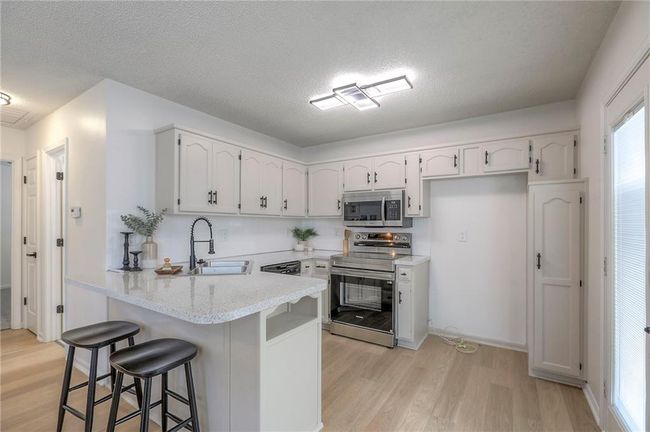 Kitchen featuring a peninsula, appliances with stainless steel finishes, white cabinets, light wood-style flooring, and a breakfast bar area | Image 7