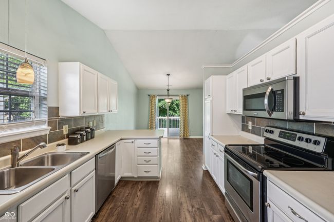 kitchen with appliances with stainless steel finishes, lofted ceiling, dark wood finished floors, and white cabinets | Image 15