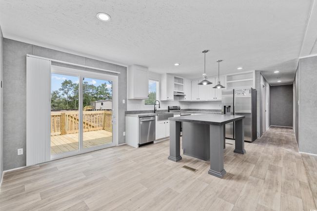 Kitchen featuring stainless steel appliances, open shelves, a kitchen breakfast bar, white cabinets, and dark countertops | Image 14