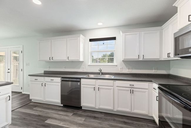 Kitchen with stainless steel appliances, a sink, white cabinets, dark countertops, and recessed lighting | Image 9