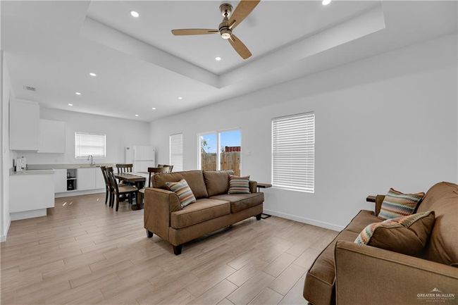 Living room with ceiling fan, a raised ceiling, and light wood-type flooring | Image 13