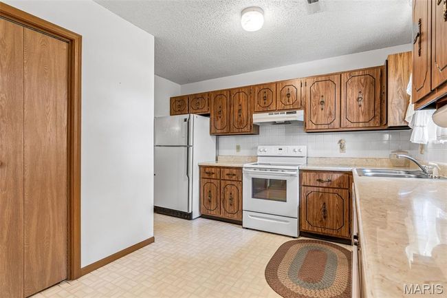 Kitchen with white appliances, under cabinet range hood, a sink, brown cabinets, and light countertops | Image 16