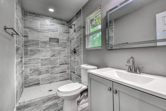 Bathroom featuring a tile shower, vanity, a textured wall, and recessed lighting | Image 17